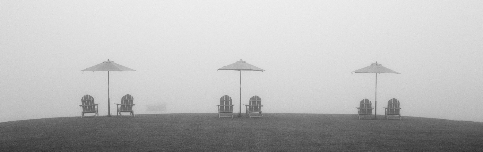 Adriondack chairs and umbrellas on a foggy lawn.