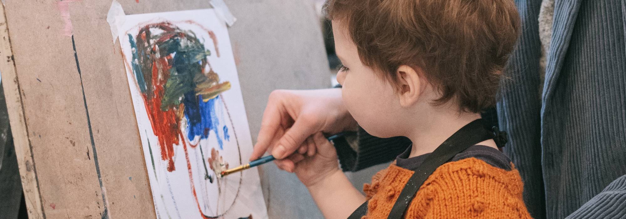 A child painting with guidance from an adult, using vibrnat colors on a large sheet or paper
