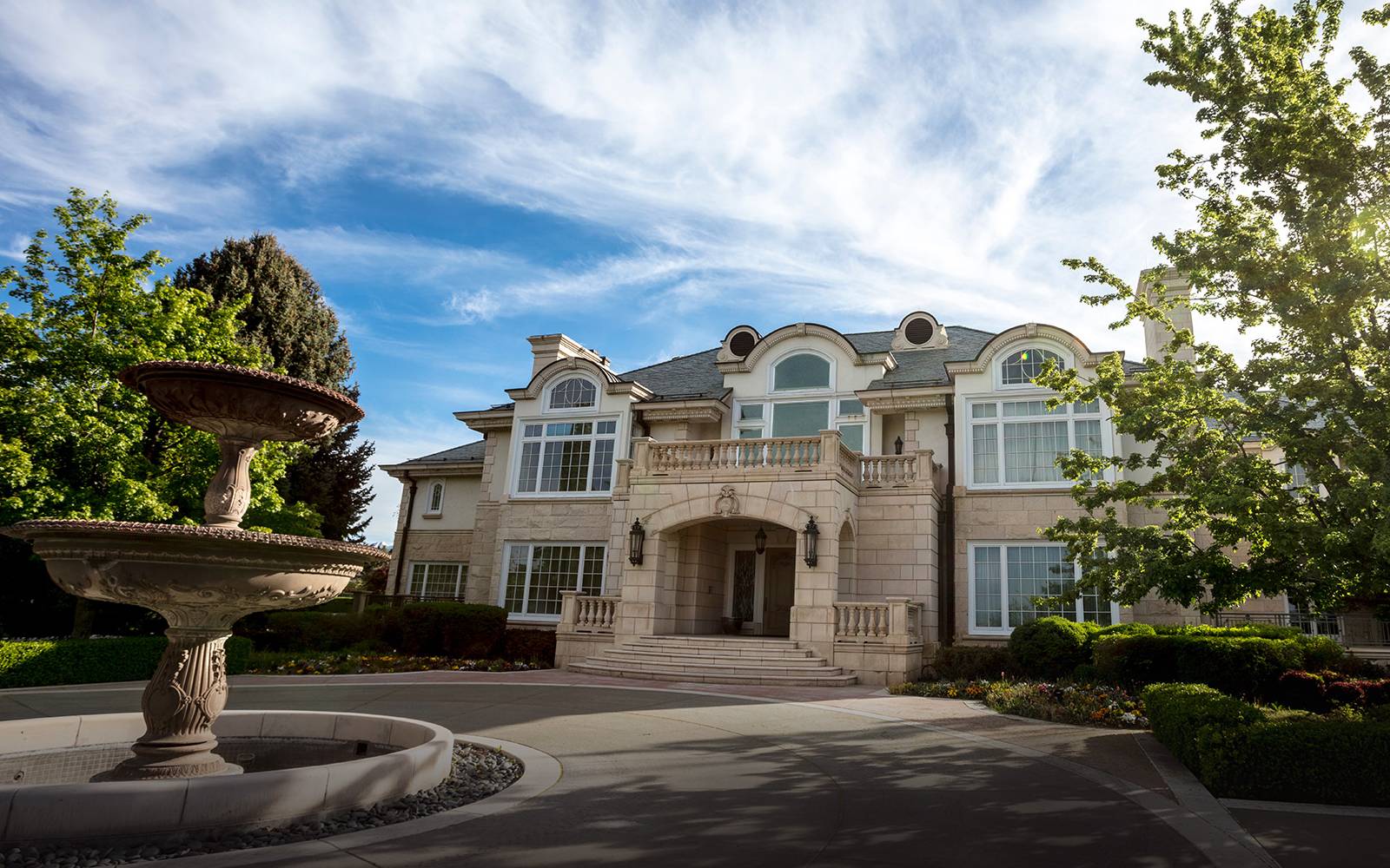 Elegant mansion with arched windows and a central entrance, flanked by a two-tiered stone fountain in a ga理查德·道金斯en setting.              