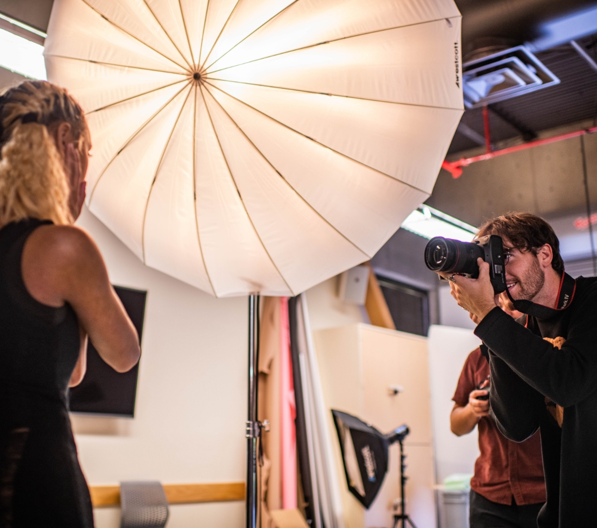 A photographer taking a picture in a studio with a large umbrella light.              