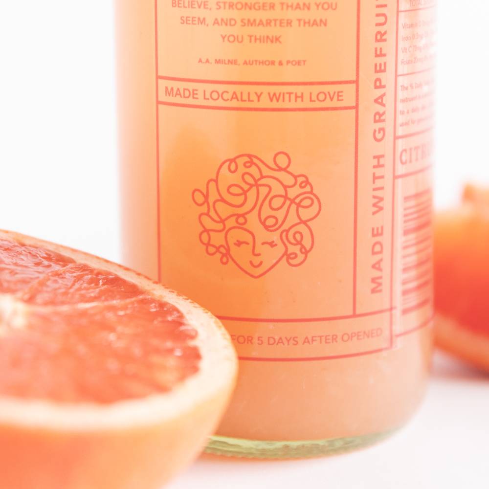 Close-up of a juice bottle with an orange-pink label and a grapefruit half.              