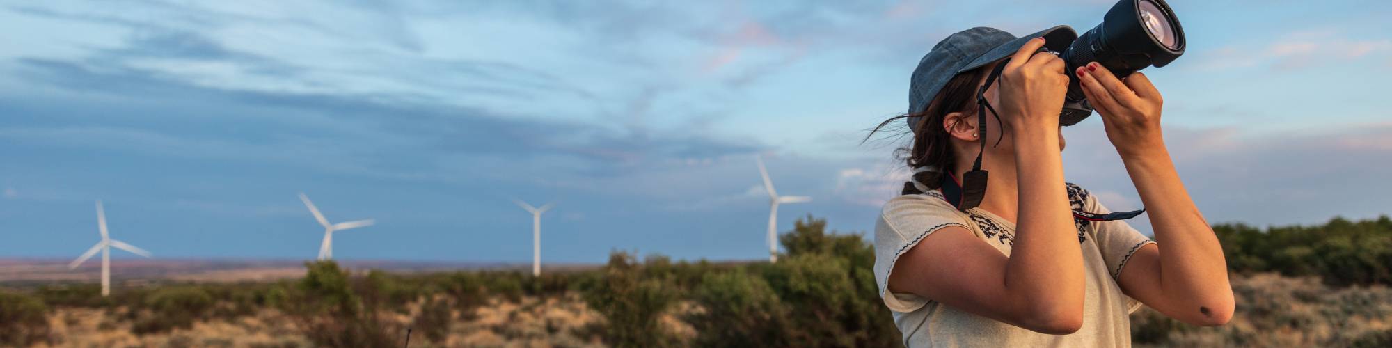 Person with a camera photographing outdoors with wind turbines in the background.              