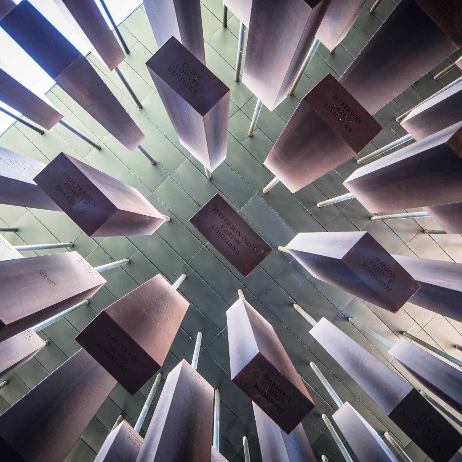 Hanging rust-colored metal prisms with inscriptions against a pale green ceiling.              