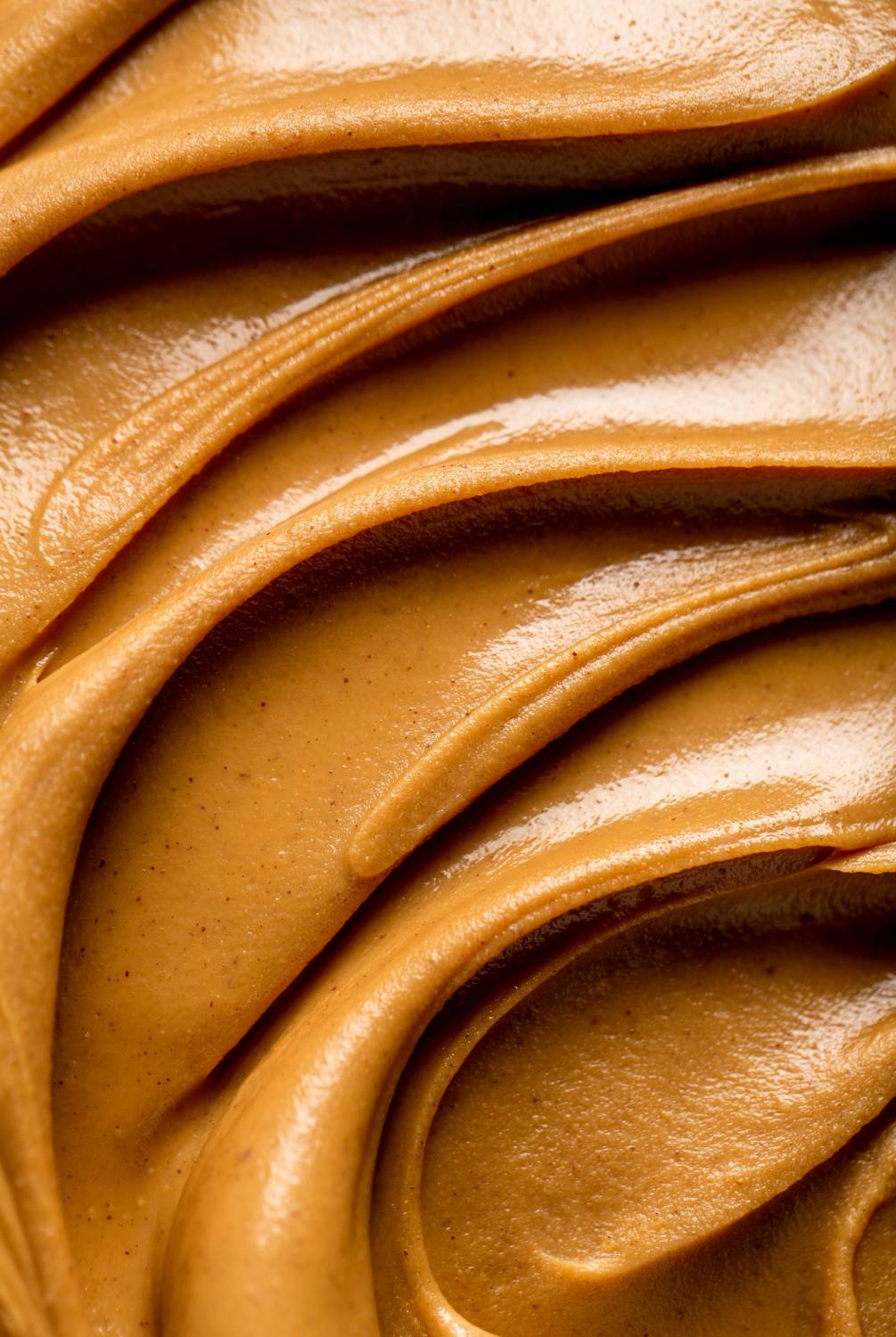 Close-up of smooth peanut butter with swirls and a glossy texture.              