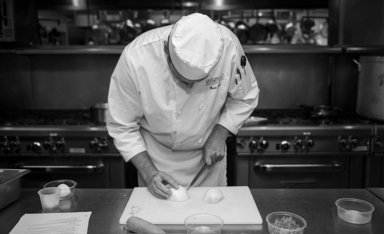 Chef slicing an onion on a cutting board in a professional kitchen.              