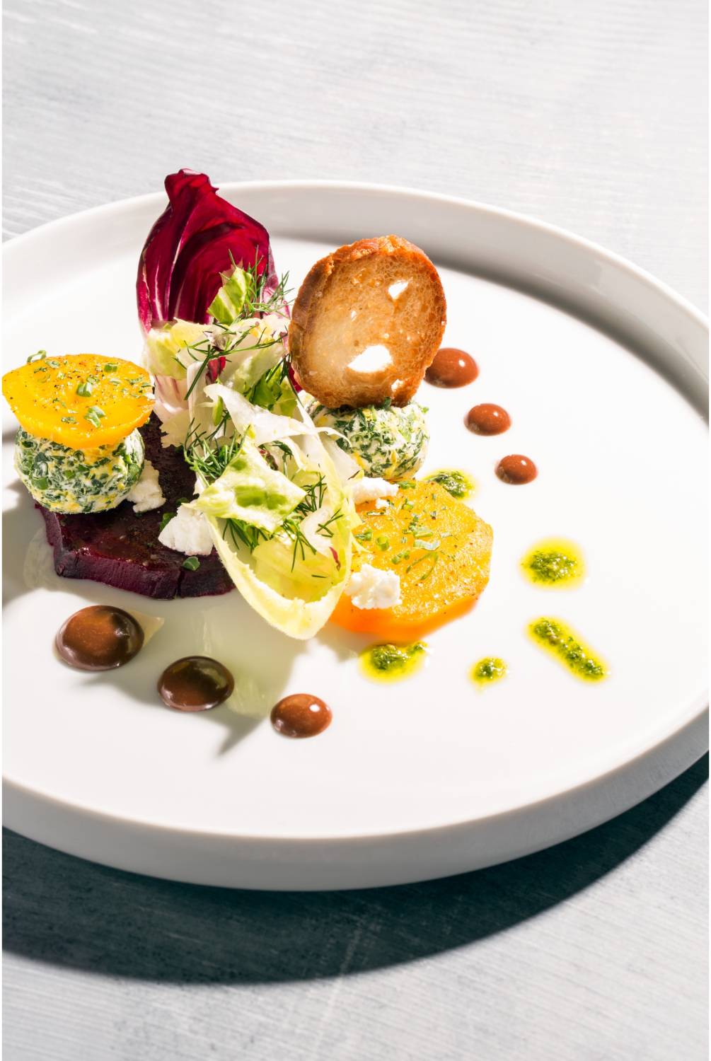 A gourmet dish with beets, spinach mousse, a bread crisp, and various colorful sauces and garnishes on a white plate.              