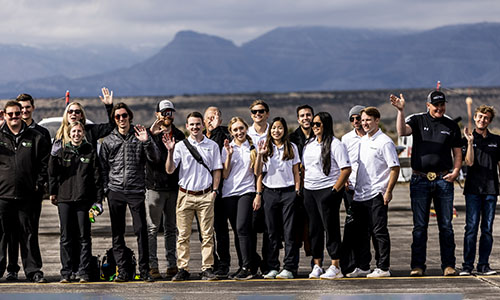 A group of students and faculty standing on a runway waving