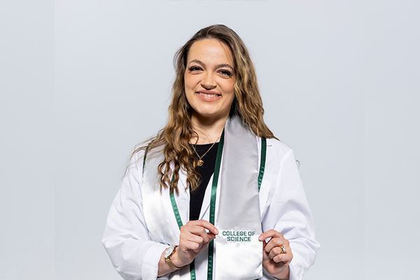 Female wearing graduation clothing, showing stole with "理学院" written on it. 