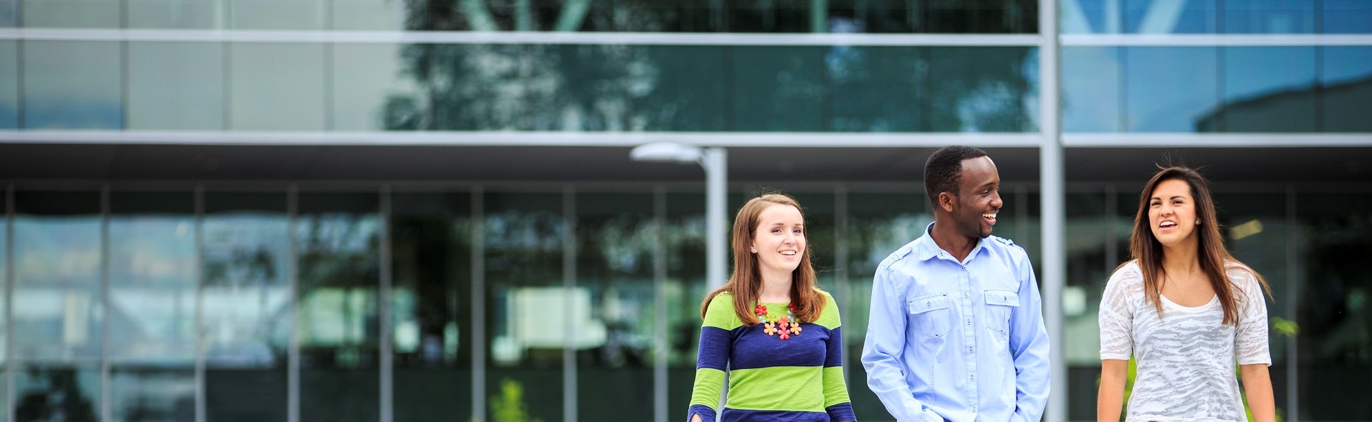 Three students smiling and walking in front of glass building.