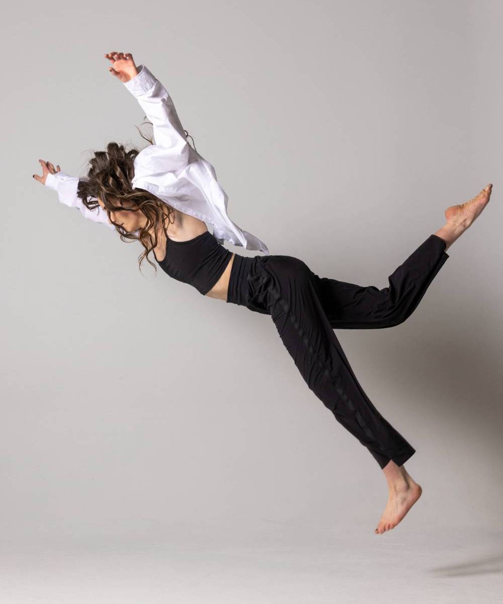 Person in a mid-air wearing a white shirt and a black outfiit against a gray backgrorund 