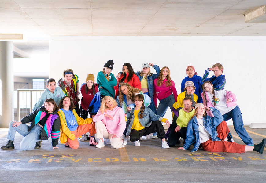 A group of people posed energetically in a parking garage, wearing colorful casual clothing.              