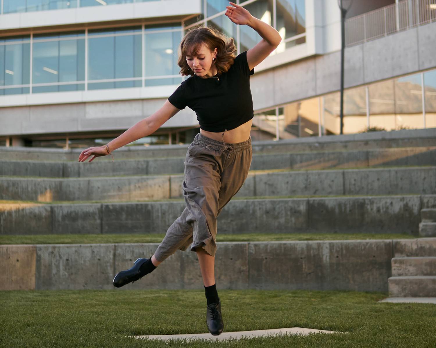 A person dancing on grass in front of a building with concrete steps.              