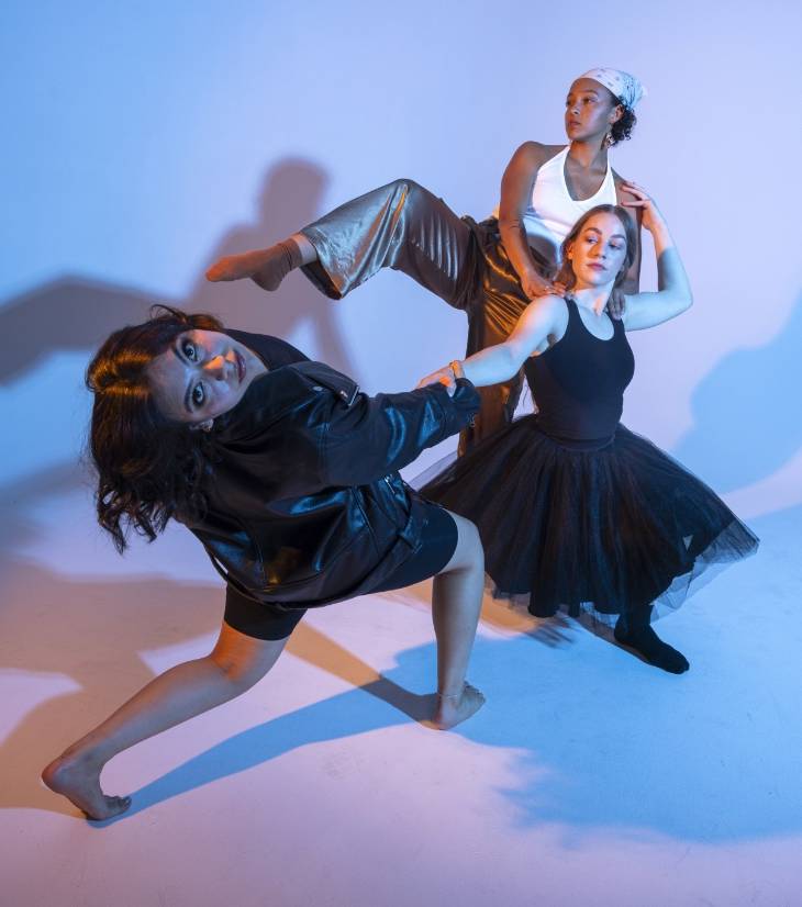 Three dancers in dynamic poses with a blue-lit backdrop.              