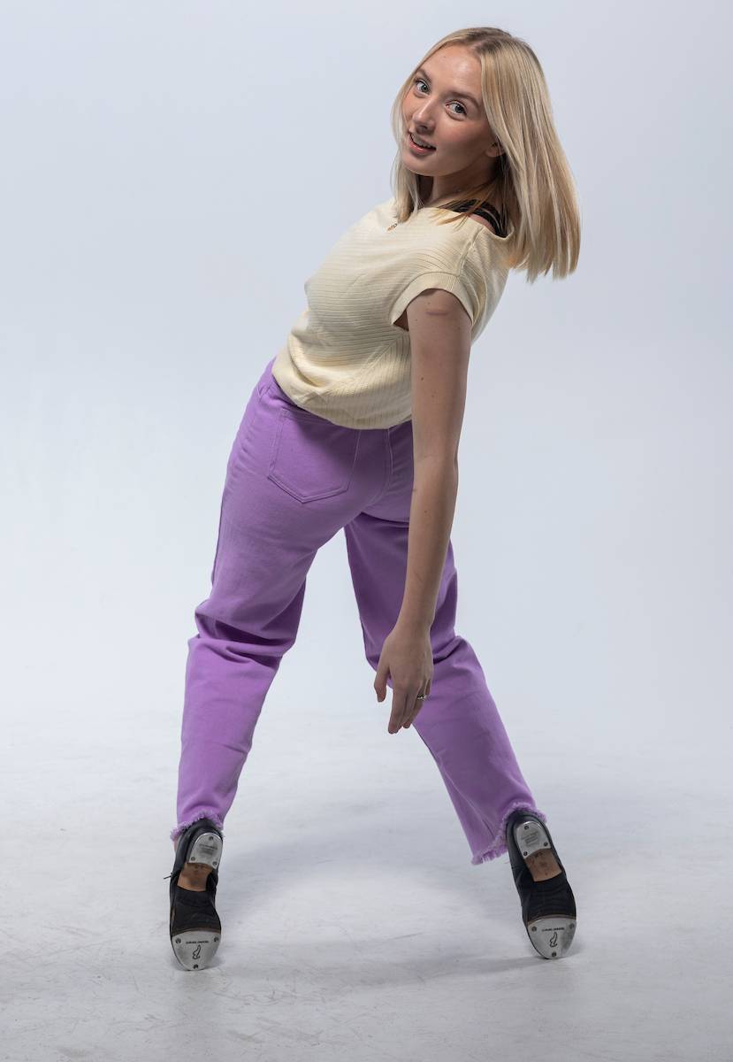 Person in a yellow top and lavender pants posing with tap shoes.              
