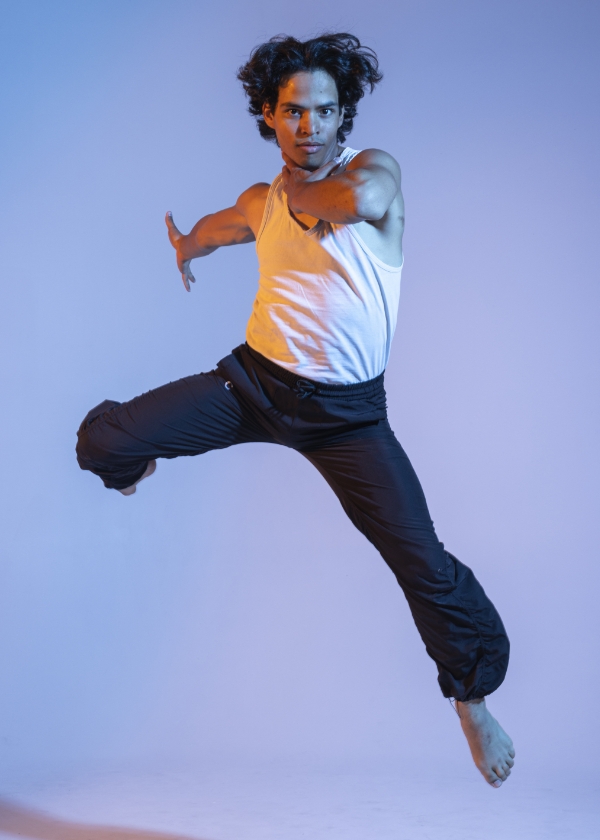 A person in mid-air wearing a white sleeveless shirt and black pants against a blue and purple gradient background.              