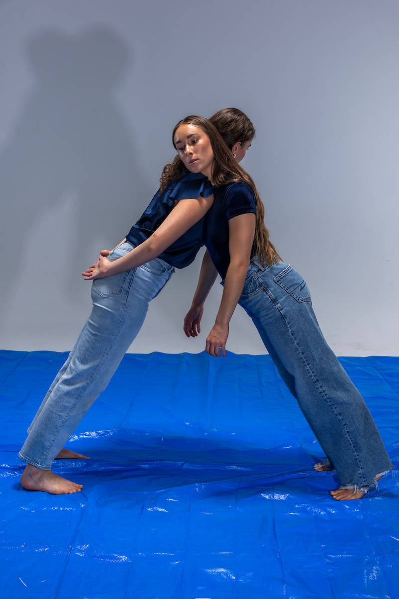 Two people in blue clothes leaning against each other on a blue tarp.              