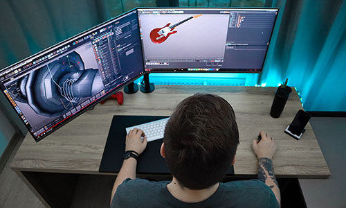 person designing a guitar on a double moniter desktop