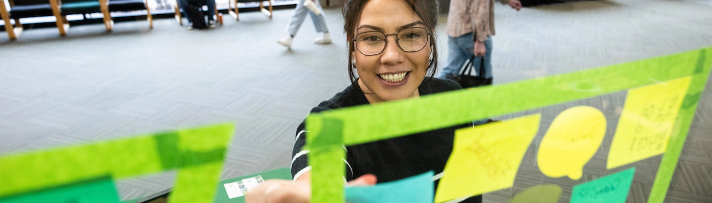 Smiling woman adding a sticky note to a window.