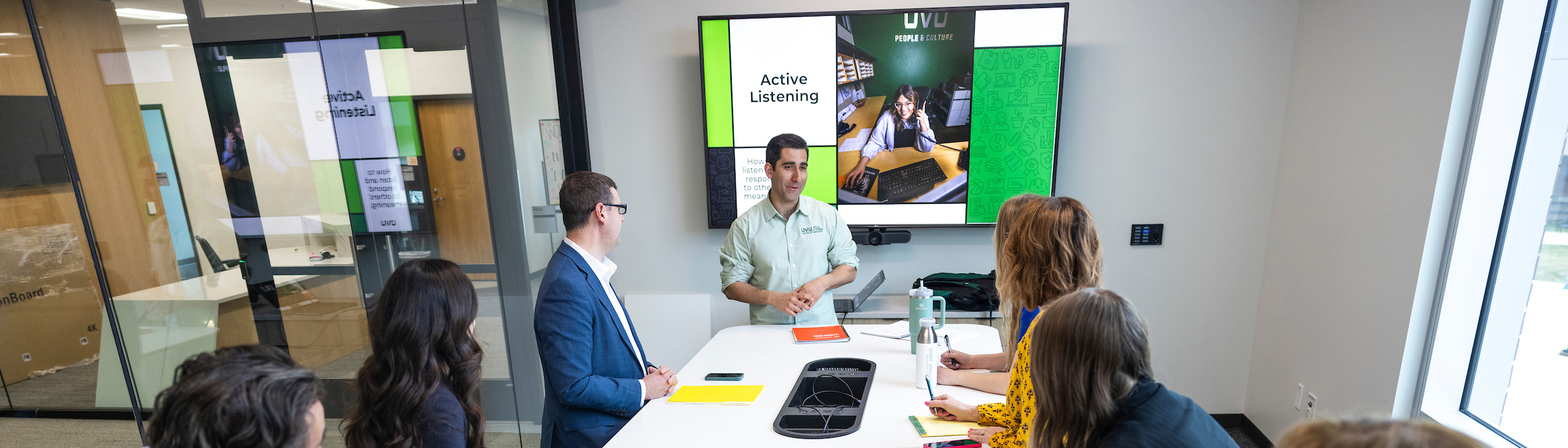 A group sitting around a conference table. One person at the front is presenting.