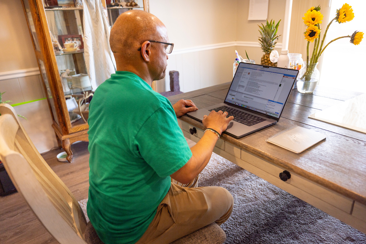 Man sitting at a desk in a home office, using a laptop computer.