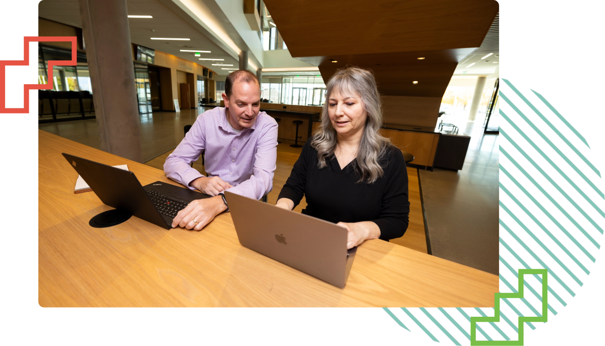 two people seated at a table with their laptops in front of them
