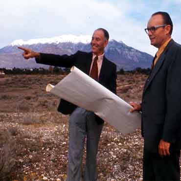 威尔逊索伦森 standing outside with another man, who is holding building plans. Wilson is pointing to a spot.