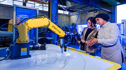 female faculty working one on one with female student and robotic arm